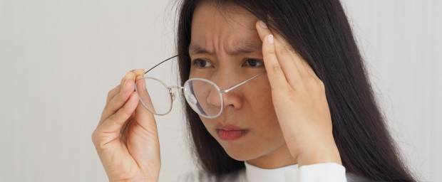 Asiatische Frau zieht ihr Brille von den Augen und fasst sich an den Kopf
