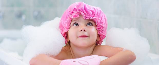Kleines Mädchen mit pinker Badekappe in Badewanne
