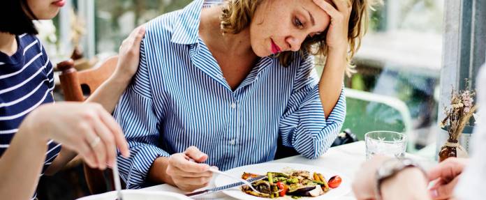 Frau mit Appetitlosigkeit sitzt vor einem Teller mit Essen