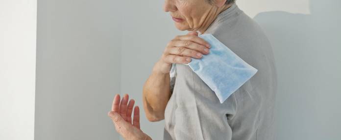 Ältere Frau mit Wärmekissen auf der Schulter als Therapiemaßnahme
