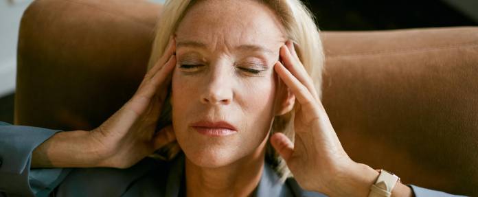 Frau mit Kopfschmerzen hält beide Hände an den Schläfen