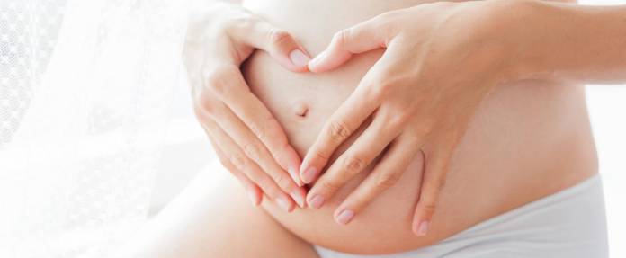 Schwangere Frau in Unterwäsche hält die Hände auf ihrem Bauch