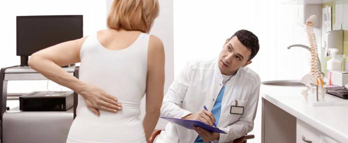 Frau mit Rückenschmerzen bei Untersuchung durch Arzt