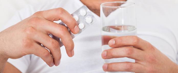 Mann mit Medikamentenblister und einem Glas Wasser in der Hand