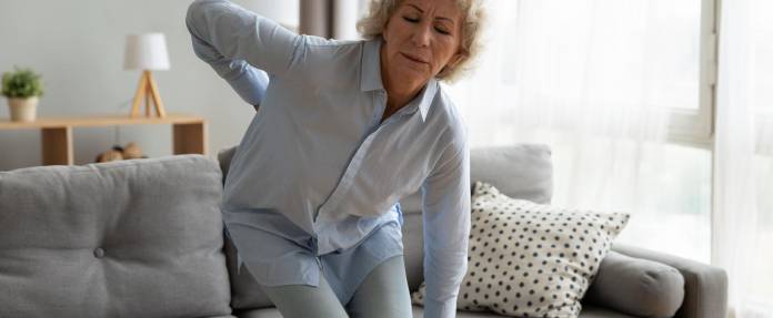 Ältere Frau mit Rückenschmerzen beim Aufstehen vom Sofa
