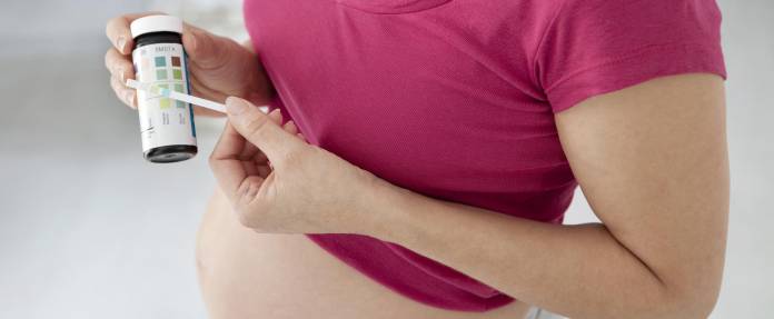 Schwangere Frau mit Urin-Teststreifen in der Hand