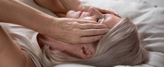 Frau im mittleren Alter liegt auf dem Bett und hält die Hände an die Schläfen