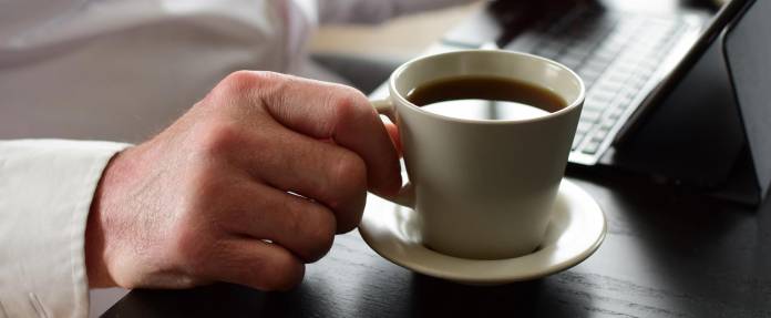 Mann mit Kaffeetasse an Laptop