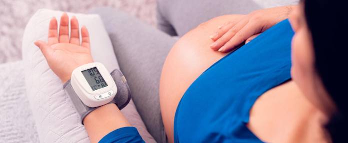 Schwangere überwacht Bluthochdruck mit Messgerät am Handgelenk