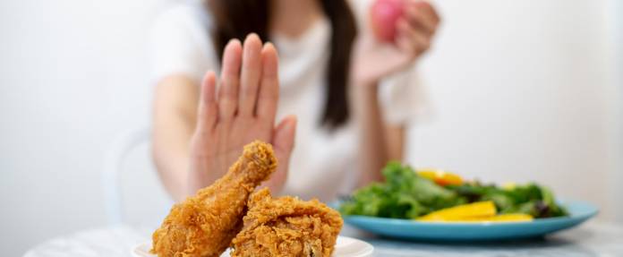 Junge Frau lehnt frittiertes Essen mit einer Handbewegung ab