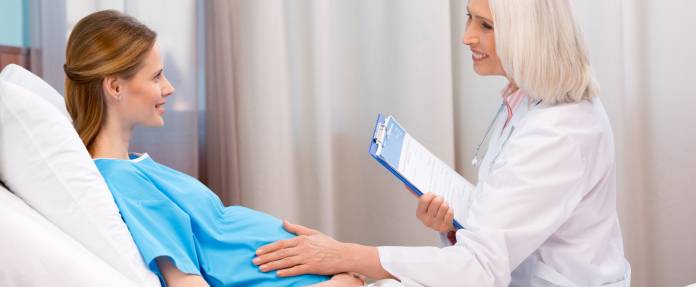 Schwangere Frau im Krankenhausbett mit Ärztin im Gespräch