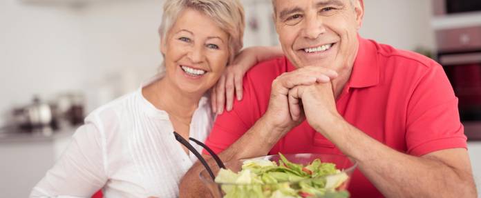 Lächelndes älteres Paar in der Küche bei Zubereitung eines Salats