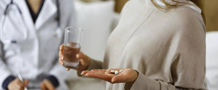 Frau mit Tabletten und Wasserglas in den Händen