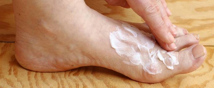 Frau cremt sich den Fuß mit Salbe ein