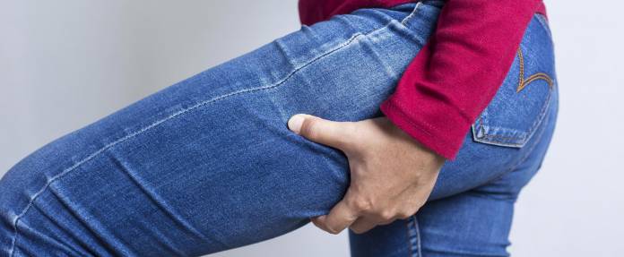 Frau fasst sich an den hinteren Oberschenkel