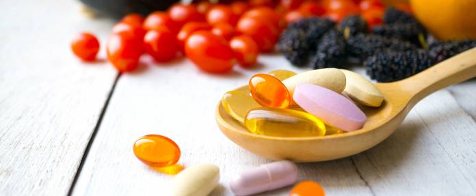 Vitaminpräparate mit Obst und Gemüse im Hintergrund
