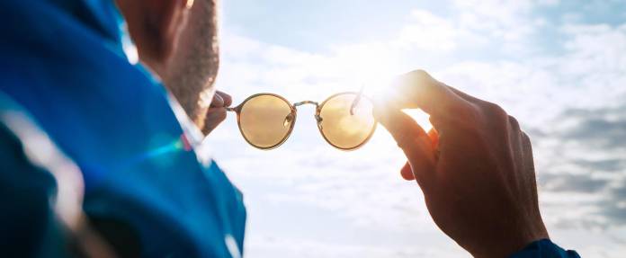 Mann hält Sonnenbrille schützend vor die Sonne