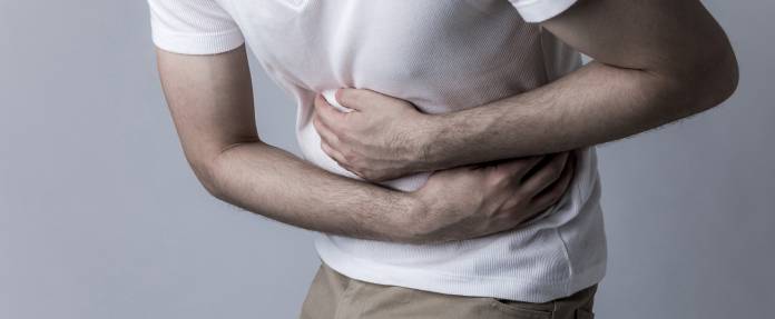 Mann krümmt sich vor Schmerzen und hält die Arme in der Seite
