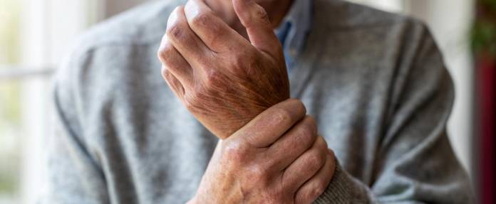 Älterer Mann umfasst sein Handgelenk