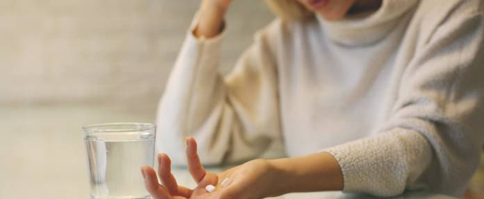 Frau mit Medikamenten in der Hand und einem Glas Wasser