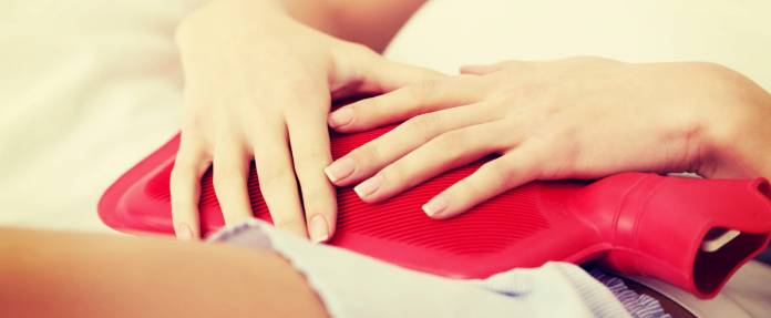 Frau mit Wärmflasche auf ihrem Bauch