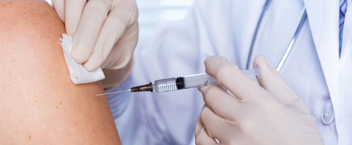 Arzt bei einer Impfung mit Spritze in den Oberarm des Patienten