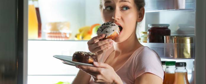 Junge Frau am Kühlschrank, die Donuts isst
