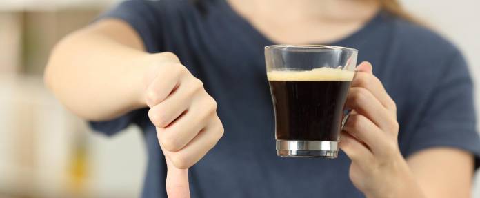 Frau mit Kaffeetasse in der Hand und die anderen Hand zeigt mit dem Daumen nach unten