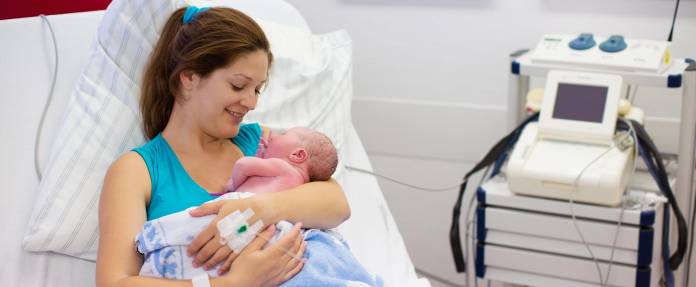 Junge Frau mit Neugeborenem auf dem Arm nach Geburt im Kreißsaal