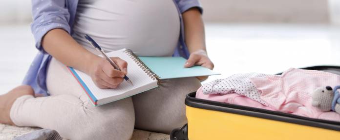 Schwangere Frau mit Checkliste packt Ihre Kliniktasche