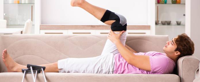 Mann mit Knieorthese macht Übungen auf dem Sofa
