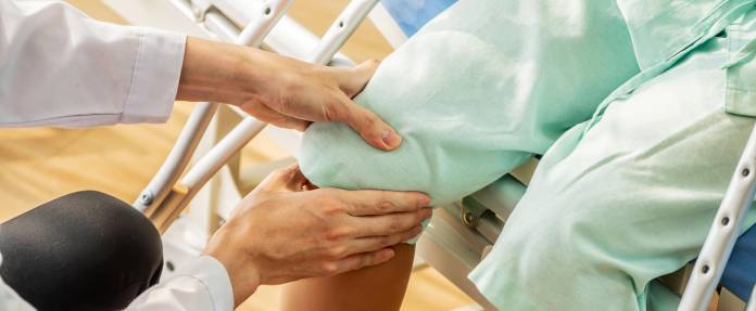 Arzt untersucht Knie einer älteren Patientin