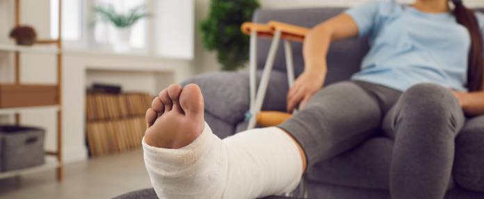 Junge Frau mit gebrochenem Bein sitzend auf dem Sofa