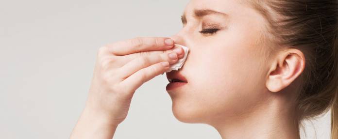 Frau mit Nasenbluten hält sich Taschentuch an die Nase