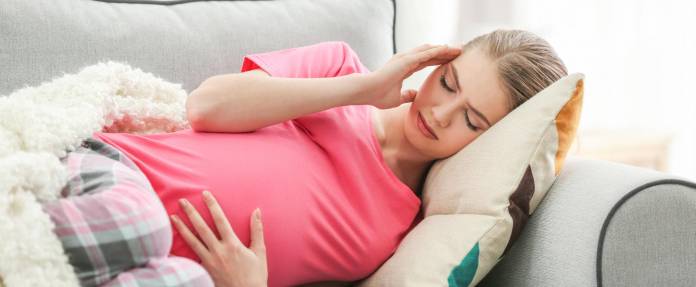 Schwangere Frau mit Kopfschmerzen liegend auf dem Sofa