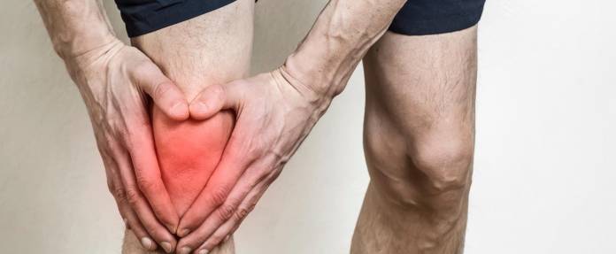 Mann hält sich das rot eingefärbte Knie wegen Schmerzen