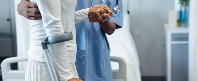 Frau übt im Krankenhaus mit Hilfe auf Unterarmgehstützen zu laufen