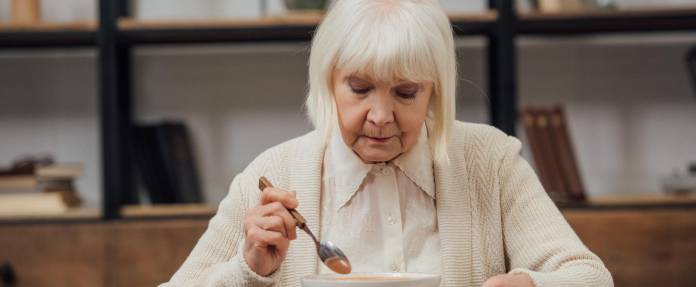 Ältere Frau isst alleine einen Teller Suppe