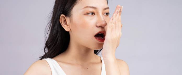 Junge Frau hält sich die Hand vor dem Mund wegen Mundgeruch