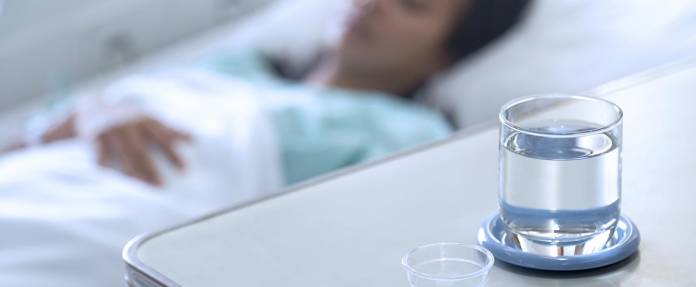 Asiatische Frau im Krankenhausbett mit Medikamenten und Wasser am Bett