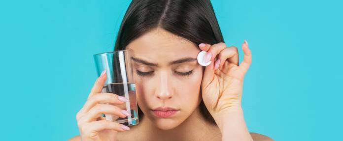 Frau mit Kopfschmerzen hat Tablette und Wasserglas in der Hand