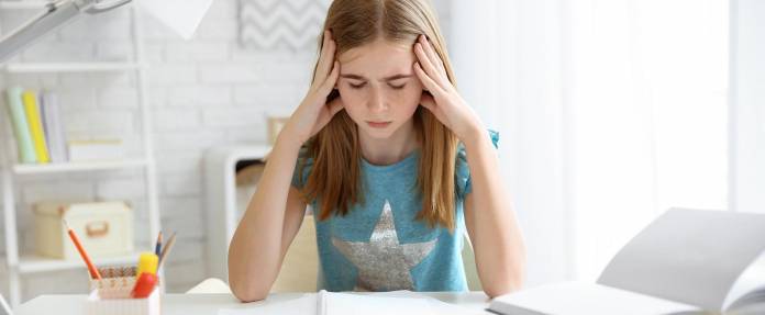 Junges Mädchen mit Kopfschmerzen beim Hausaufgaben machen