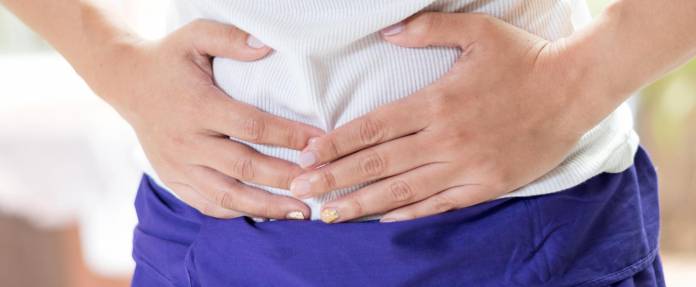 Frau fasst sich mit beiden Händen an den Bauch wegen Schmerzen im Magen-Darm-Bereich