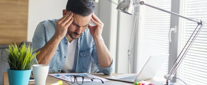 Junger Mann hält sich den Kopf am Arbeitsplatz