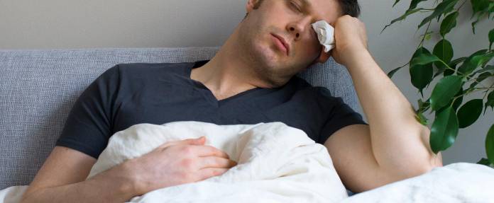 Mann liegt im Bett und fühlt sich krank