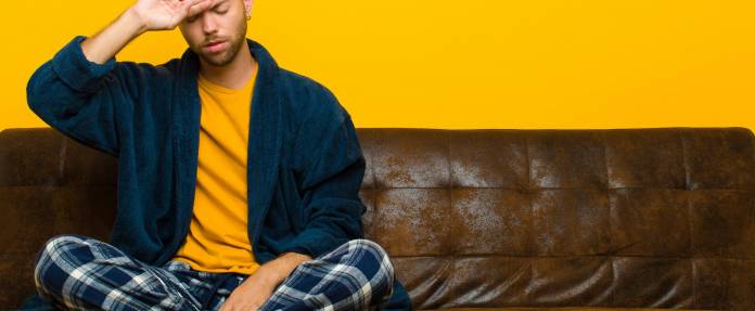 Junger Mann sitzt im Schlafanzug schwitzend auf dem Sofa