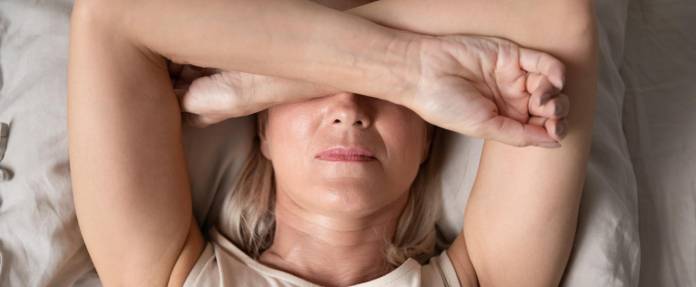 Ältere Frau liegt mit verschränkten Armen über dem Kopf im Bett