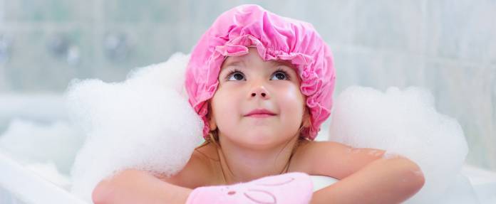 Kleines Mädchen mit pinker Badekappe in Badewanne
