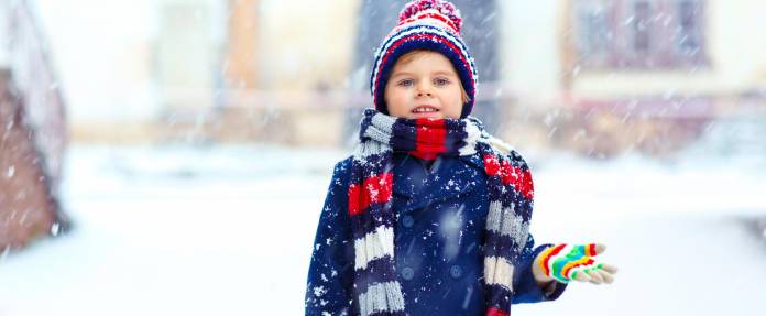 Junge im Schnee dick angezogen mit Mütze, Schal und Handschuhen
