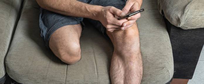 Mann mit amputiertem Unterschenkel sitzt auf einem Sessel und schaut ins Handy
